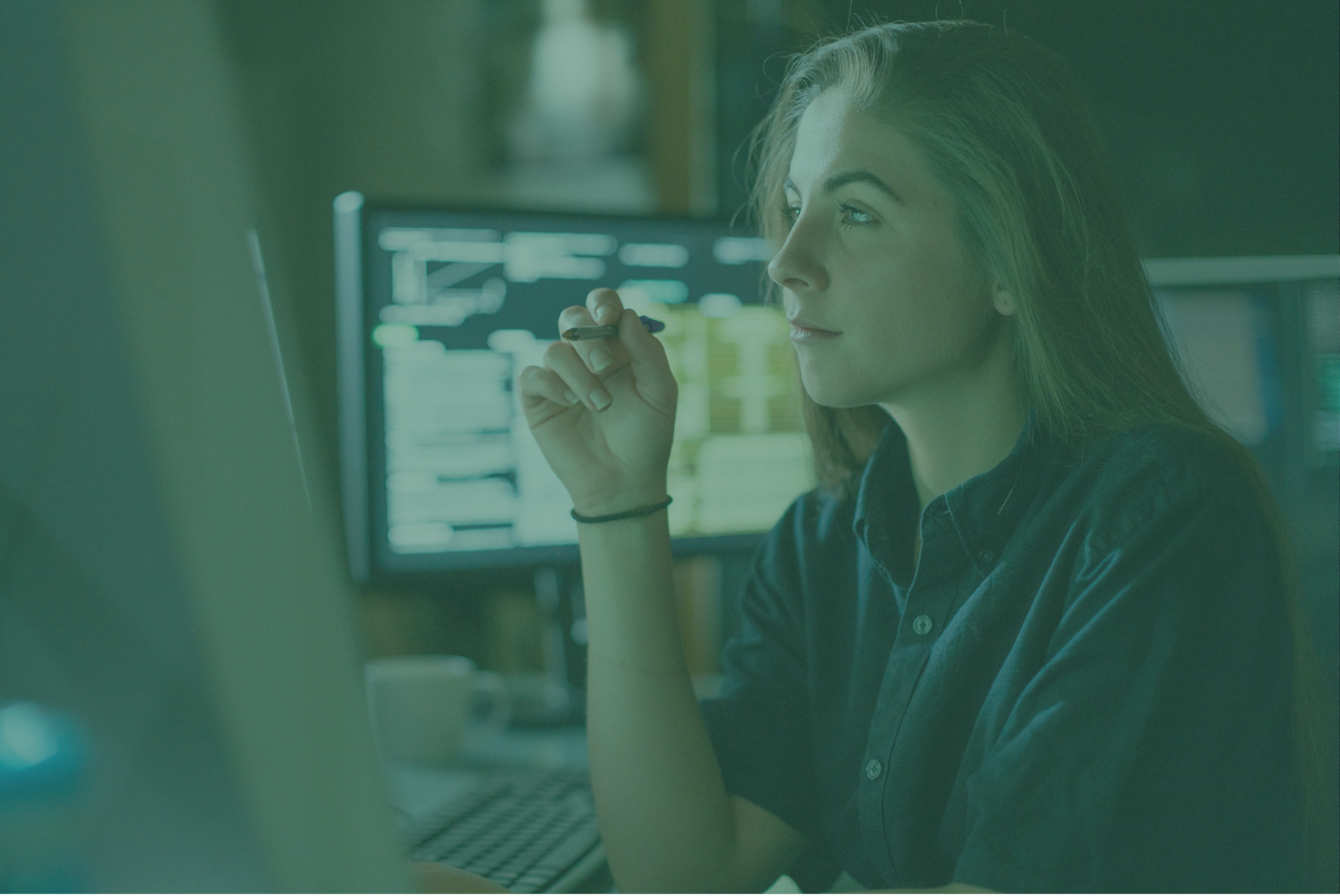 a person holding a pen sitting at a desk. In the background there is a computer screen.