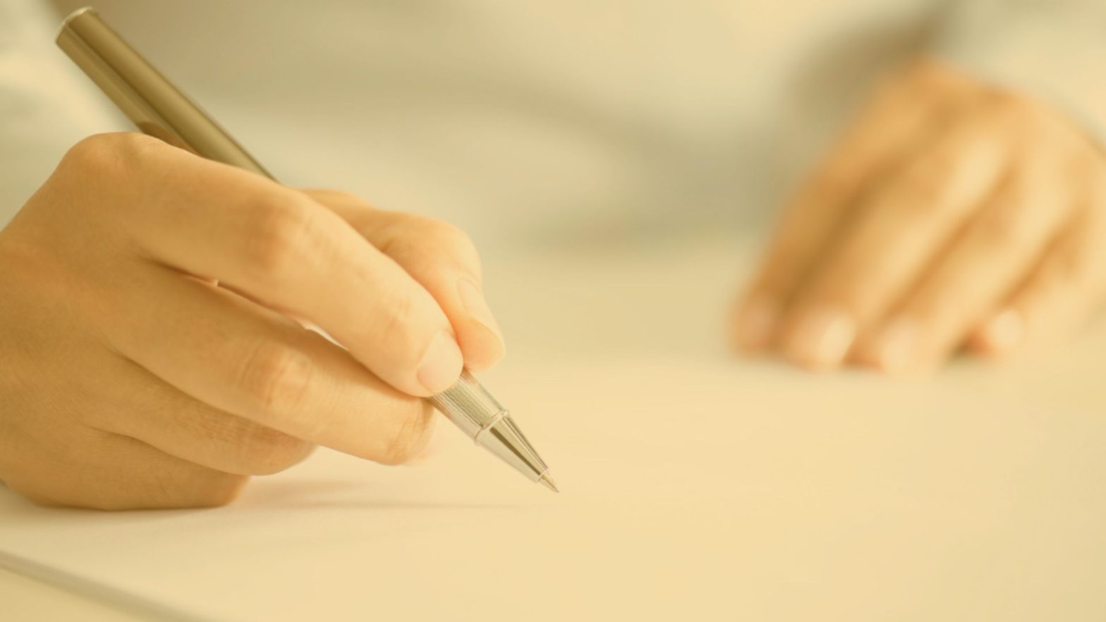 A hand holding a pen is writing on paper.