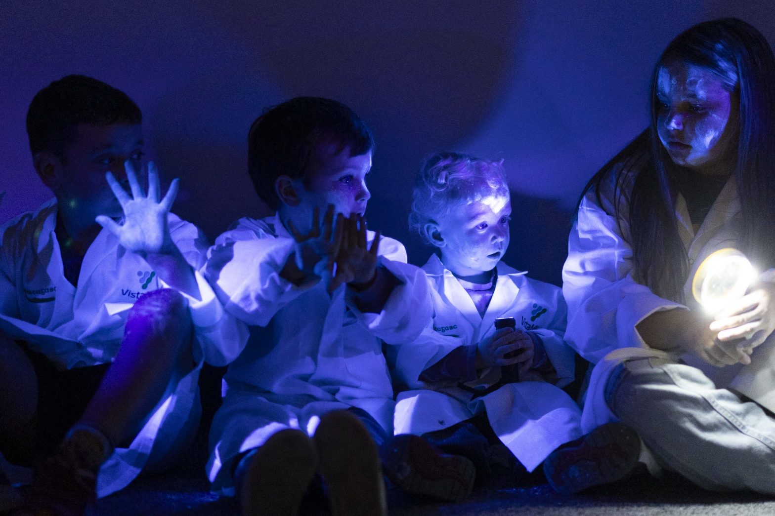 A pciture of a group of children in lab coats playing with lights.